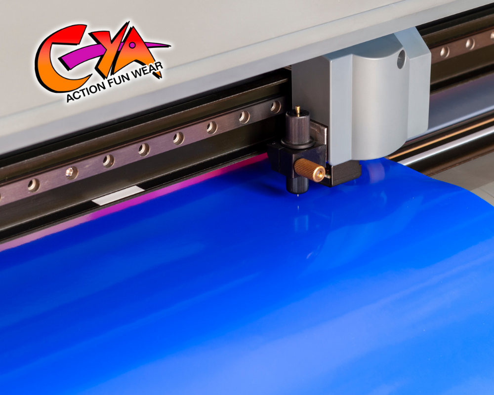 A vinyl cutter machine prints and cuts blue vinyl material; the CYA TEES Action Fun Wear logo appears in the upper left corner.